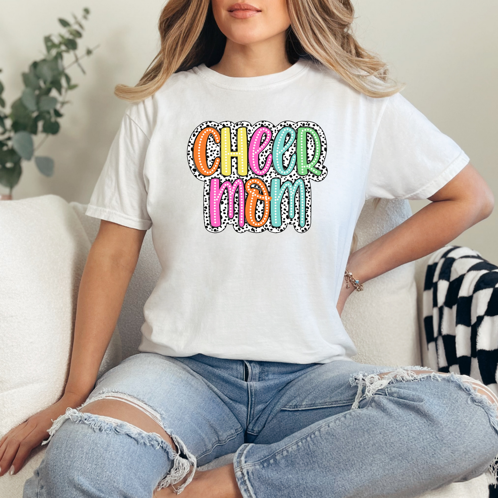 Cheer mom shirt in the color white with a bright doodle style font with a background behind the words that appears like black and white dalmatian dots.