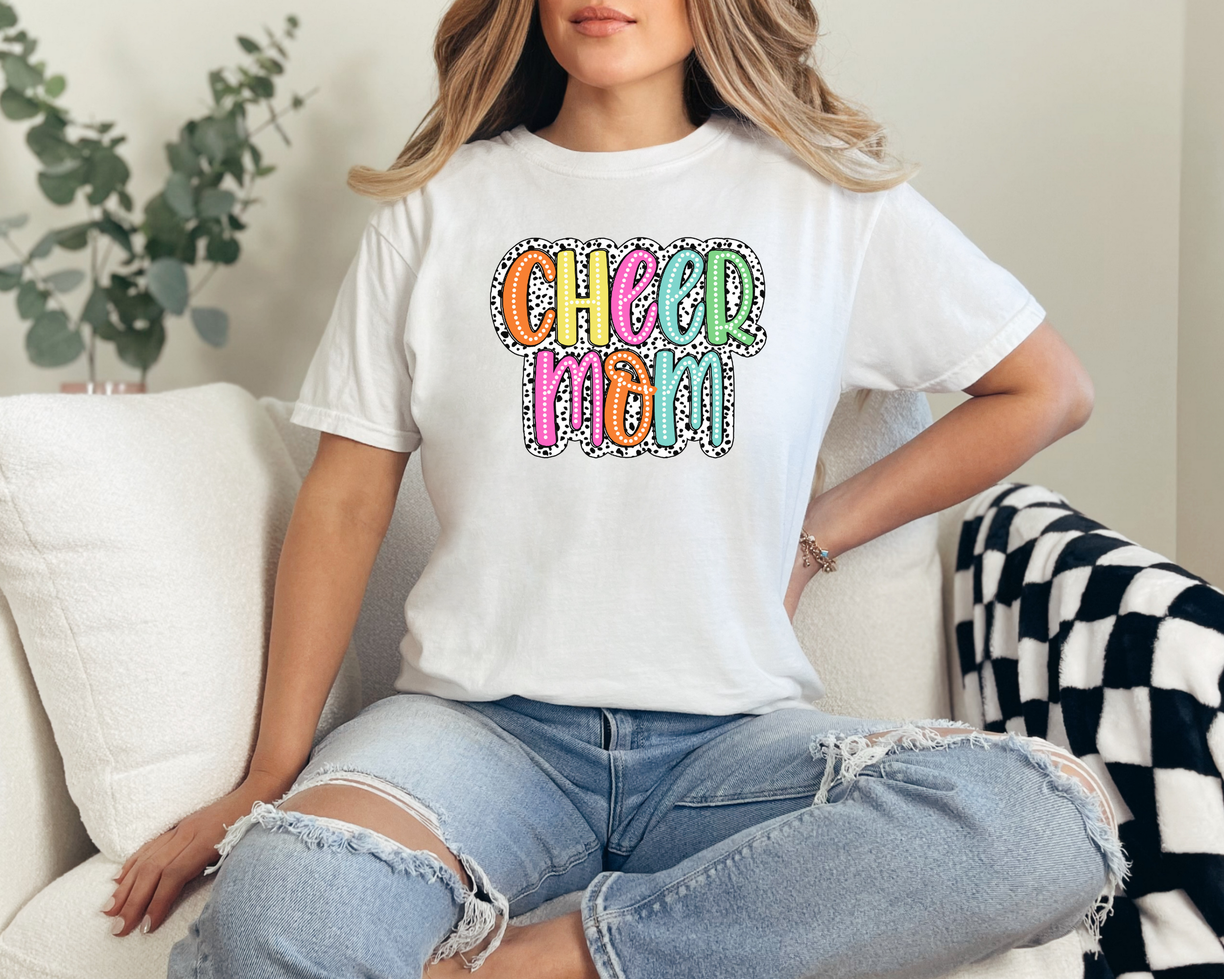 Cheer mom shirt in the color white with a bright doodle style font with a background behind the words that appears like black and white dalmatian dots.