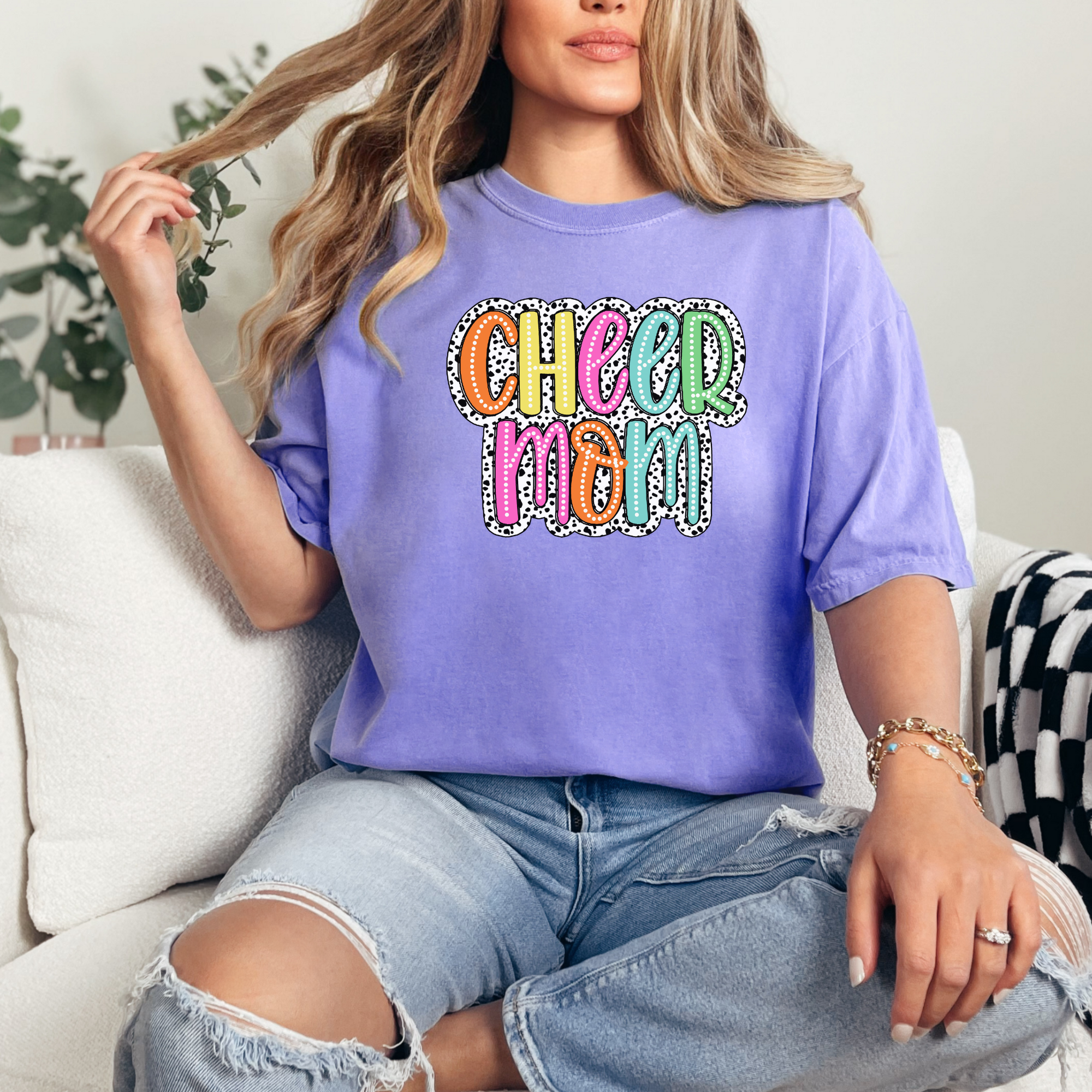 Cheer mom shirt in the color violet with a bright doodle style font with a backgroung behind the words that appears like black and white dalmatian dots.