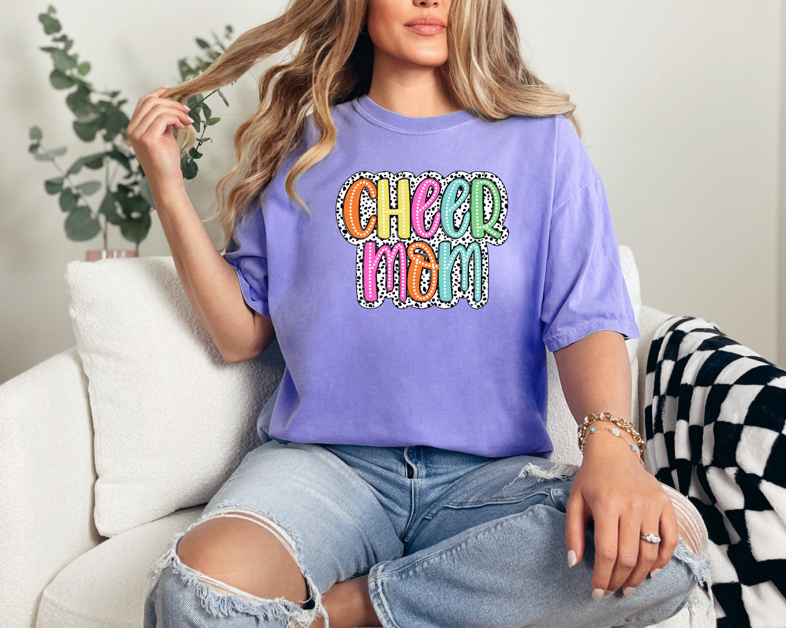 Cheer mom shirt in the color violet with a bright doodle style font with a backgroung behind the words that appears like black and white dalmatian dots.