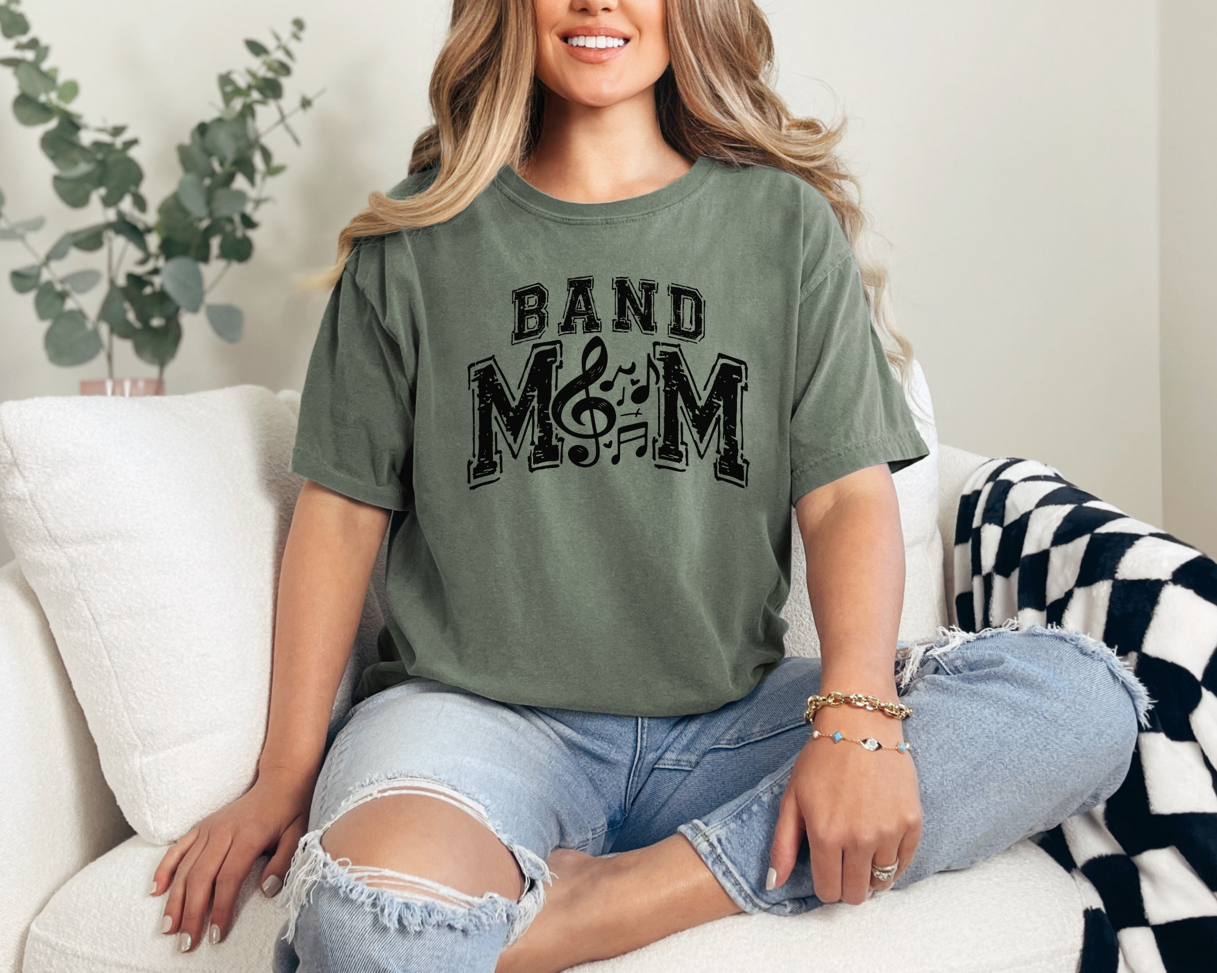 band mom tshirt in the color moss. The design is black and meant to look slightly faded in sports and where the O would be in mom its replaced with music symbols.