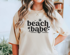 beach shirt made with ivory comfort colors tshirt with black design that says beach babe.  Subtle wave, palm tree, sun, and bird outlines around the words.