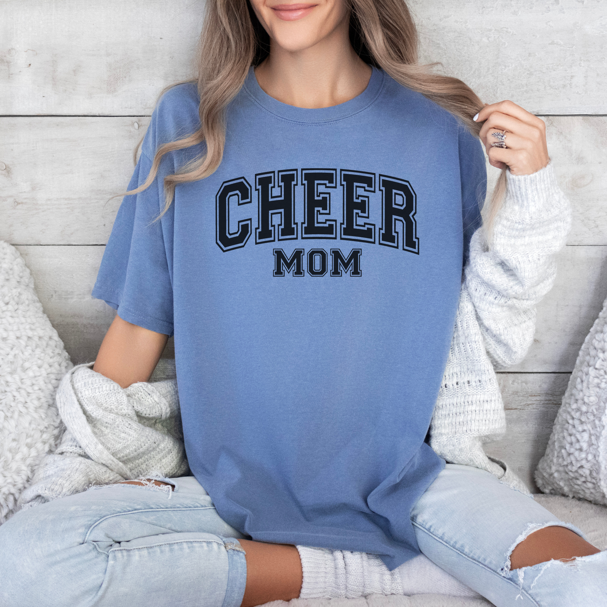 Cheer mom shirt in a college outline text in the color blue with a black design.