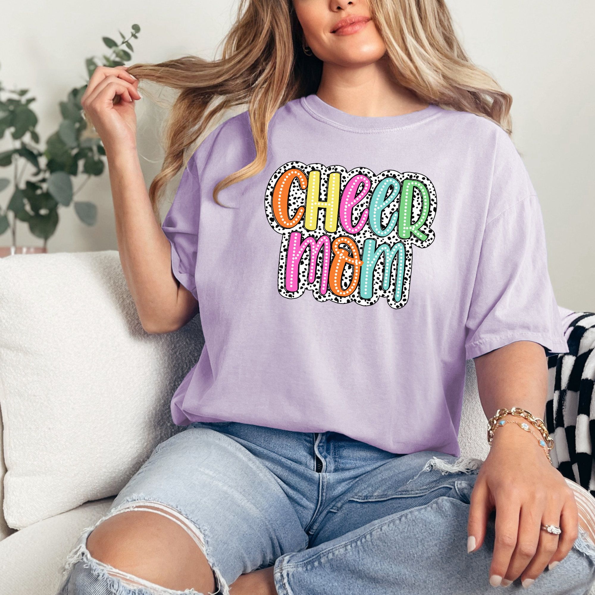 Cheer mom shirt in the color orchid with a bright doodle style font with a background behind the words that appears like black and white dalmatian dots.