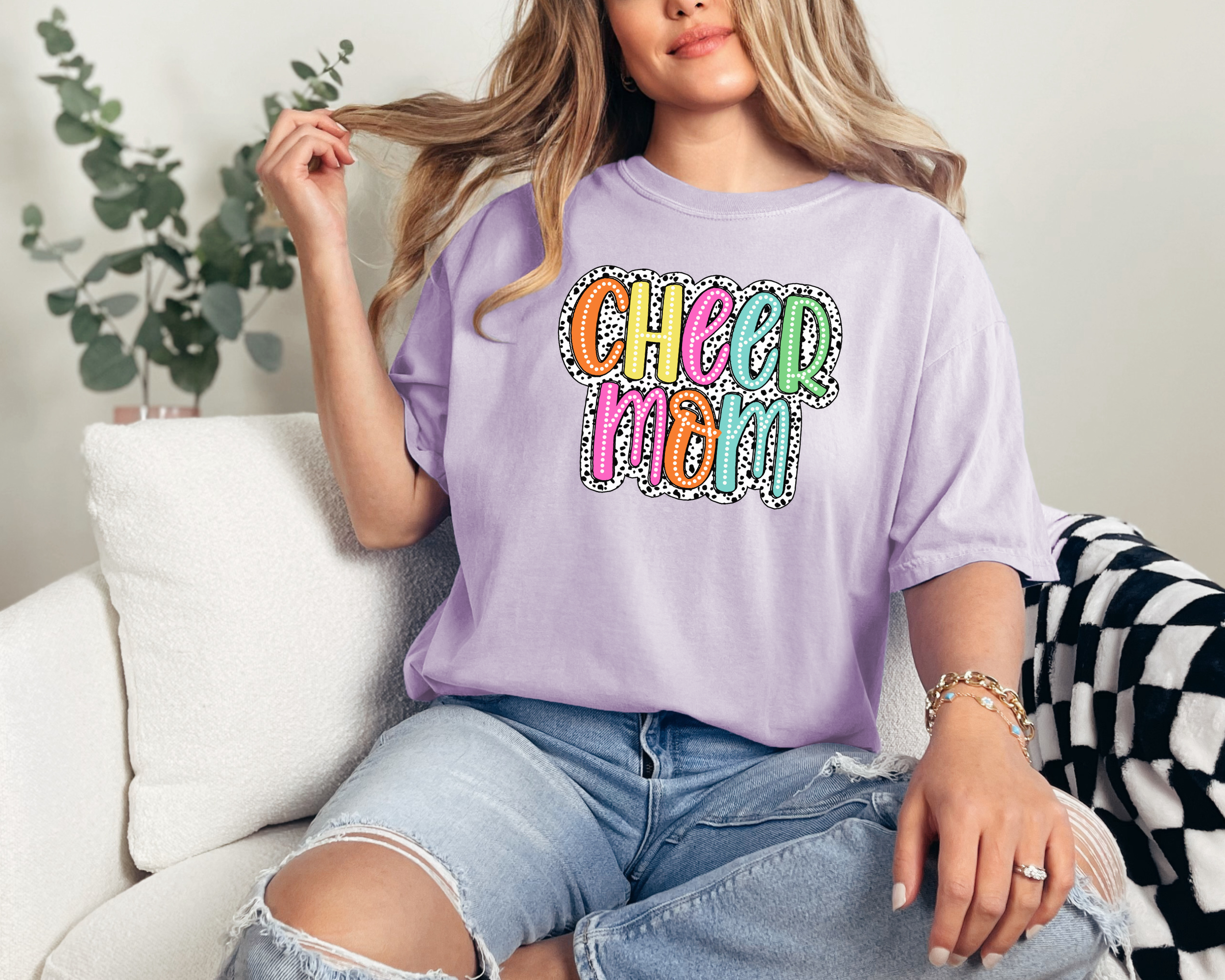 Cheer mom shirt in the color orchid with a bright doodle style font with a background behind the words that appears like black and white dalmatian dots.