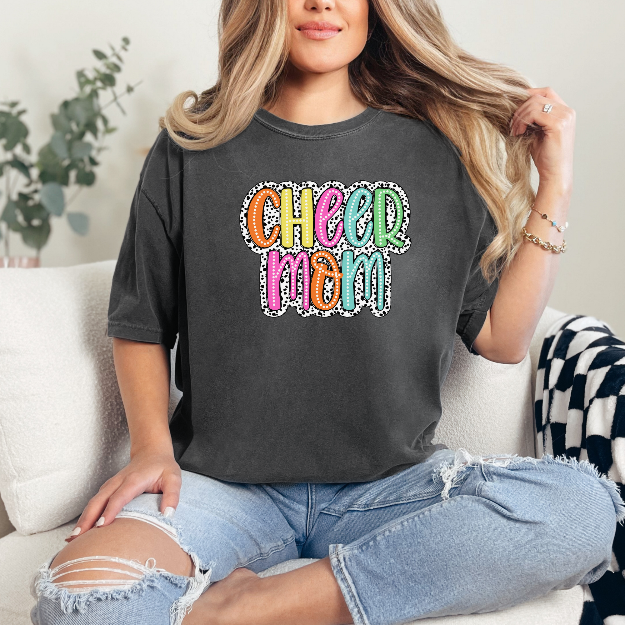 Cheer mom shirt in the color pepper with a bright doodle style font with a backgroung behind the words that appears like black and white dalmatian dots.