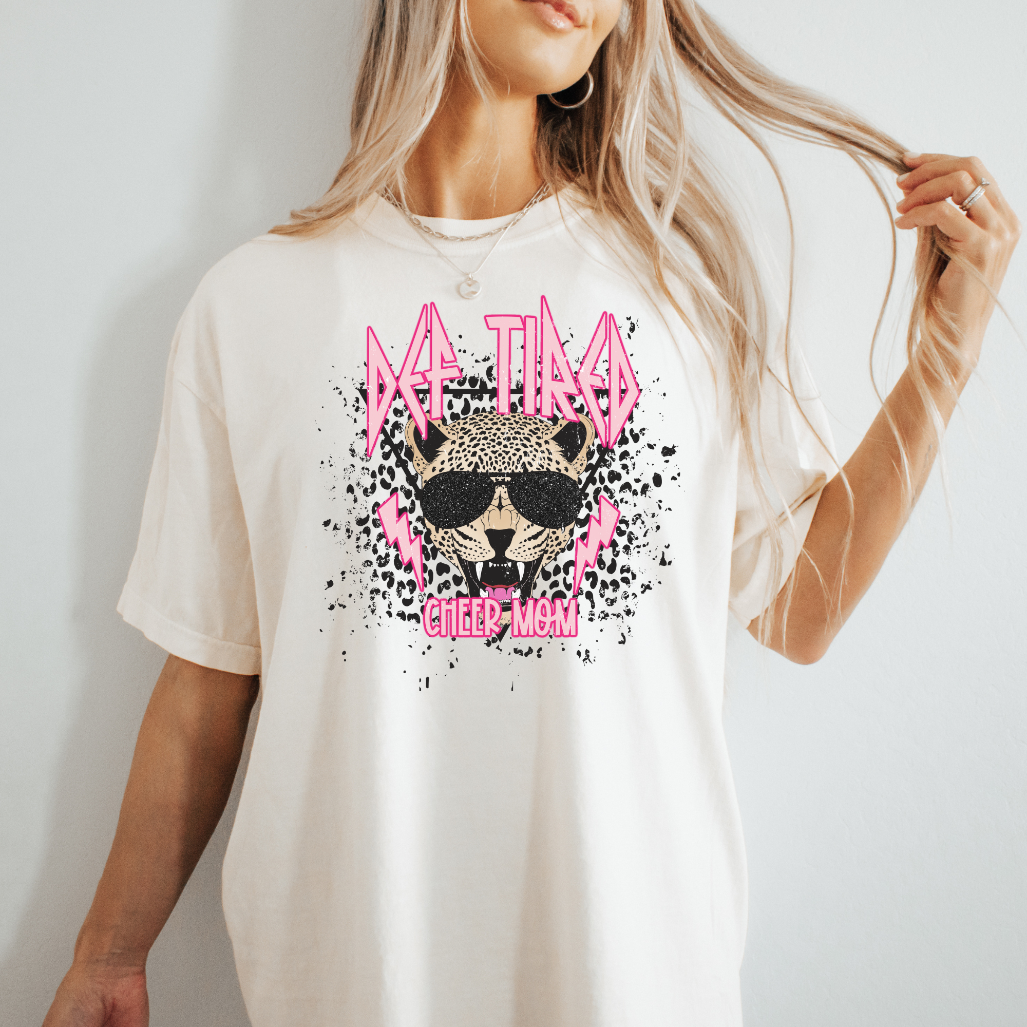 def leopard themed cheer mom tshirt.  The cheer mom graphic tee says def tired cheer mom in pink letting with a leopard head in the middle.