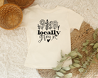 Cute kids graphic tee in the color natural with a black design.  The design is wildflowers and below it says locally grown with a heart below it.  The shirt is great for spring or summer.