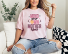 blossom colored (light pink) mom graphic tee with a 90s theme design.  The design says mind your own motherhood in pink, checkered black and white and a yellow melting smiley face.  There are also two small daisies.