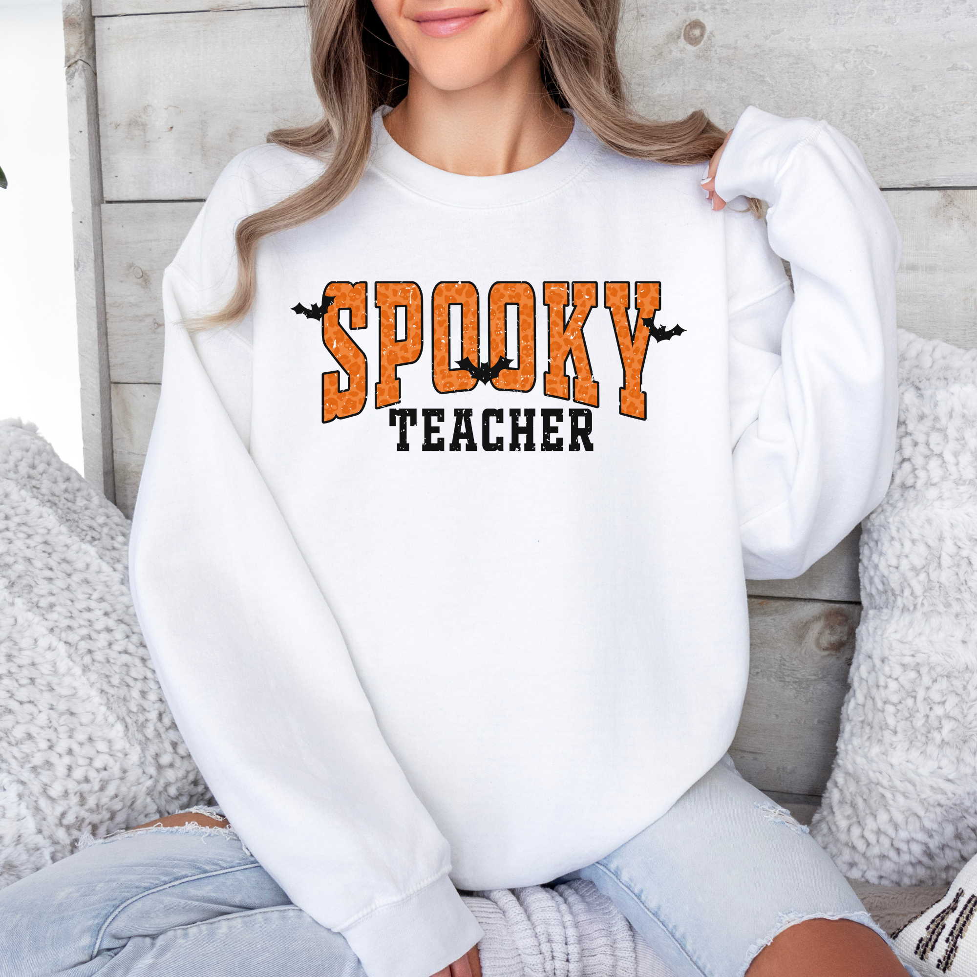 Orange Spooky teacher design on a crewneck sweatshirt in the color white.