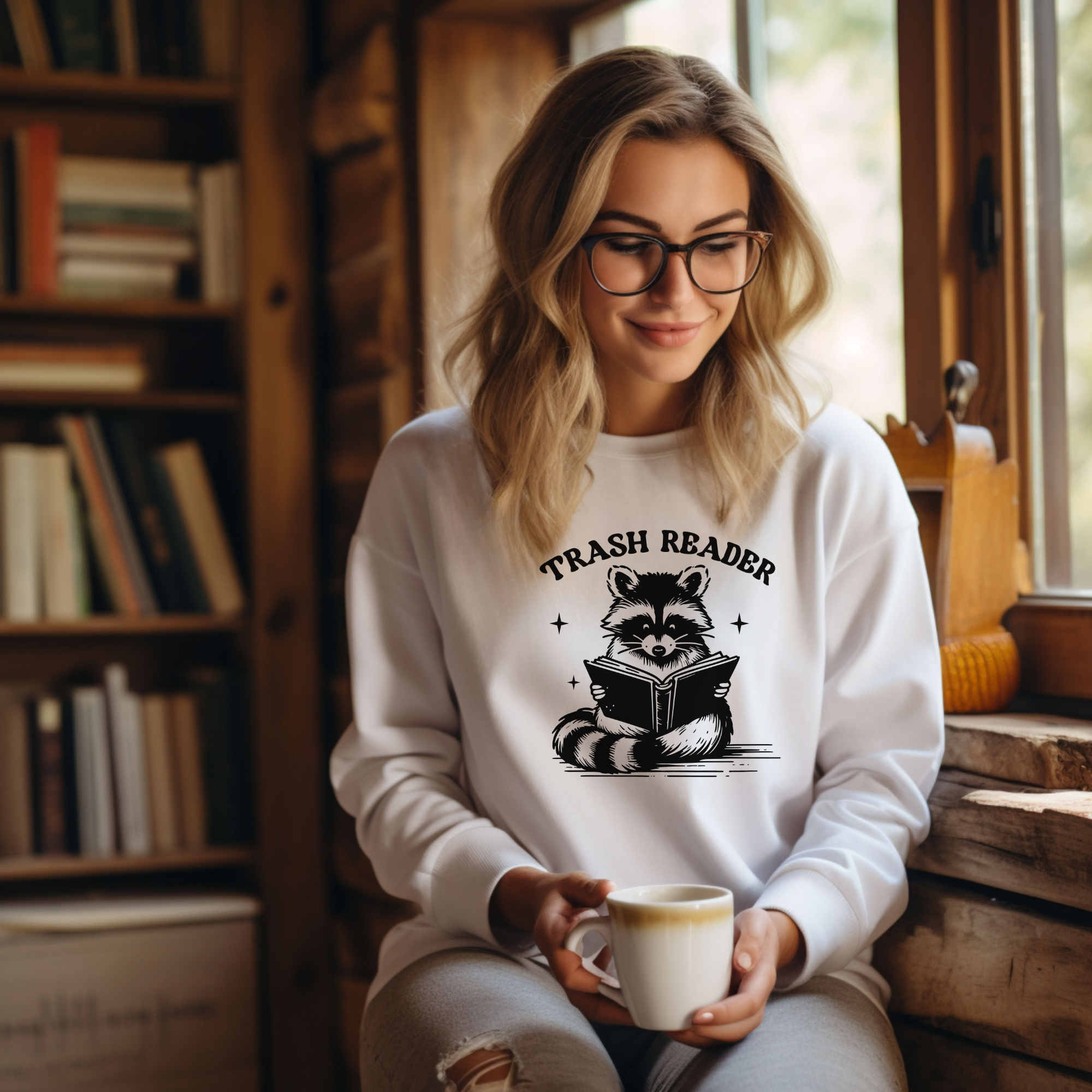 Trash reader with a raccoon reading a book.  The design is black and sweatshirt color is white.