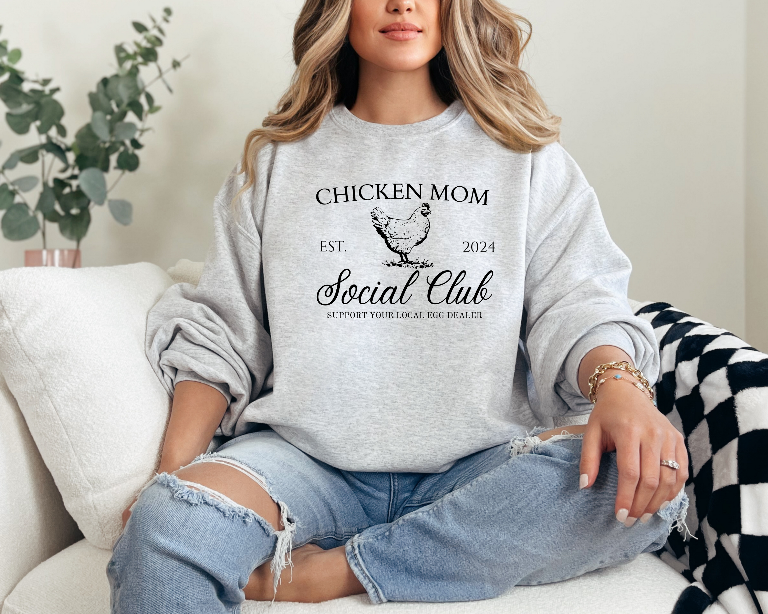 Chicken mom sweatshirt that says chicken mom social club support your local egg dealer est 2024.  The top is plain text the middle is a picture of a chicken and below says social club in fancy cursive and at the very bottom in small plain text it says support your local egg dealer