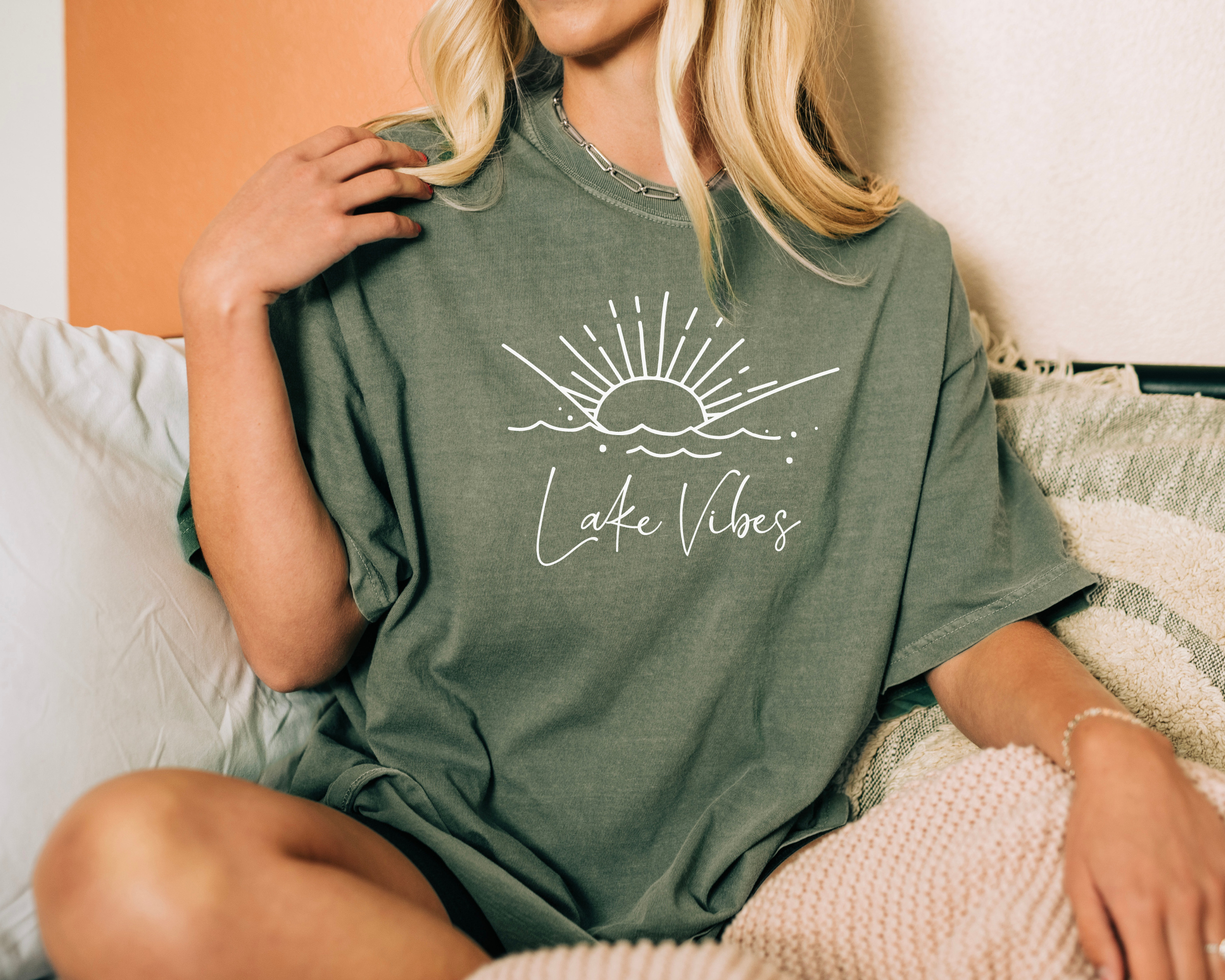 lake shirt in the color moss with a white design. The design says lake vibes in cursive and above that are simple wave lines with sun rays coming out
